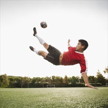 Asian soccer player in mid-air kicking soccer ball