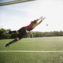 Mixed race goalkeeper in mid-air protecting goal