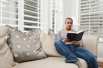Black man reading book on sofa