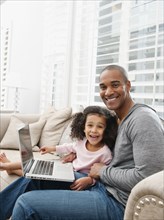 Father and daughter using laptop on sofa