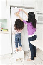 Mother putting daughter's drawing on refrigerator
