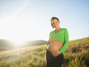 Pregnant Hispanic woman caressing stomach in field