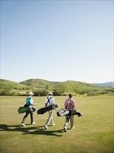 Men carrying golf bags on golf course
