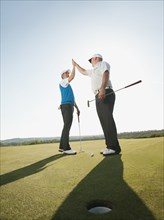 Caucasian golfers high fiving on golf course