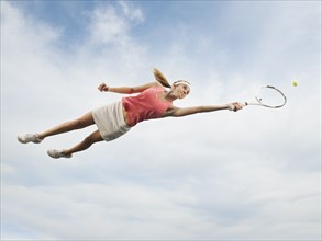 Caucasian woman jumping in mid-air playing tennis