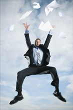 Caucasian businessman jumping in air scattering papers
