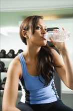 Mixed race woman drinking water in gym