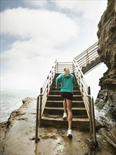 Caucasian woman running up stairs next to ocean