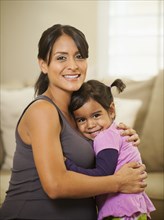 Pregnant Hispanic mother hugging daughter