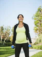 Pregnant Hispanic woman lifting weights outdoors