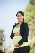 Pregnant Hispanic woman holding her belly outdoors