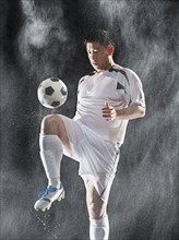 Asian soccer player kicking ball in rain