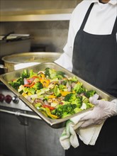Hispanic chef with tray of vegetables in kitchen