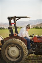 Caucasian farmer using cell phone on tractor in crop field