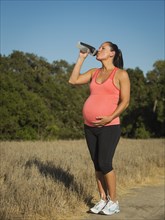 Pregnant Hispanic woman drinking water outdoors
