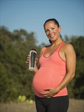 Pregnant Hispanic woman drinking water outdoors
