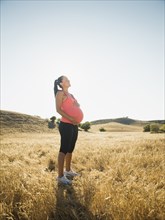 Pregnant Hispanic woman holding her belly in rural field