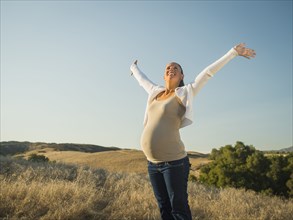 Pregnant Hispanic mother stretching in rural field