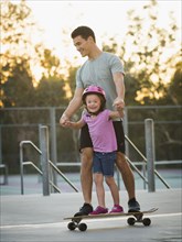 Father and daughter riding skateboard in park