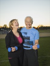 Older couple lifting weights together in urban park