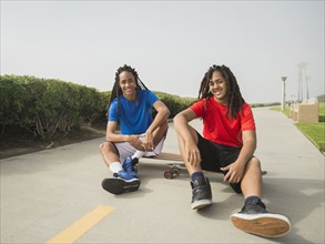 Black teenage boys sitting on skateboards on street