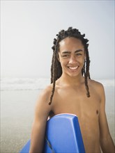 Black teenage boy carrying boogie board on beach