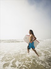 Black teenage boy carrying boogie board in waves