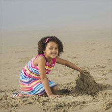 Black girl building sand castle on beach