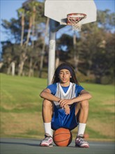 Black teenage boy sitting on basketball court