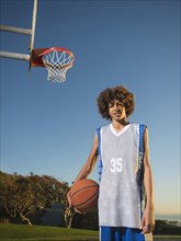 Black teenage boy holding basketball on court