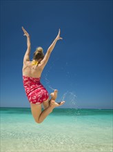 Caucasian woman jumping for joy in tropical ocean