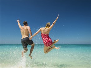 Caucasian couple jumping for joy in tropical ocean