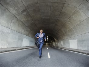 Black businessman running with briefcase in urban tunnel