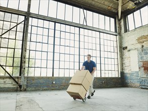 Caucasian businessman pushing cardboard boxes on hand truck in warehouse