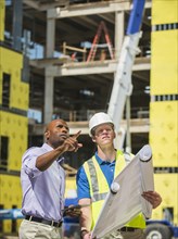 Businessman and construction worker reading blueprints at construction site