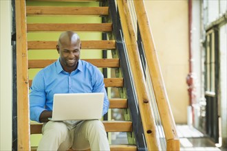 Black businessman using laptop on staircase