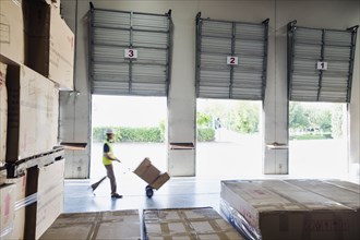 Caucasian worker wheeling cardboard boxes in warehouse