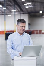 Caucasian businessman using laptop in empty warehouse