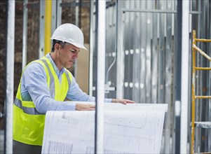 Caucasian architect reading blueprints at construction site