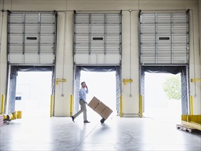 Caucasian businessman wheeling cardboard boxes in warehouse