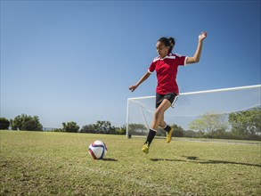 Mixed race soccer player kicking ball on field