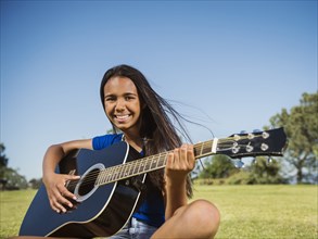 Mixed race girl playing guitar in park