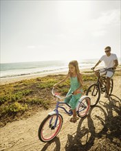 Caucasian father and daughter riding bicycles on beach