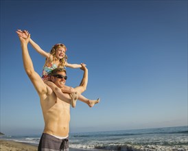 Caucasian father carrying daughter on beach