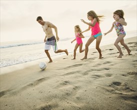 Caucasian father and daughters playing soccer on beach
