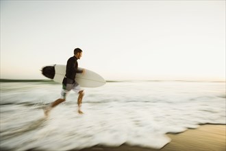 Caucasian man carrying surfboard on beach