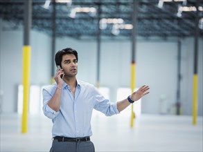 Indian businessman talking on cell phone in empty warehouse