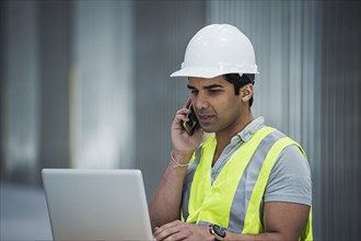 Indian worker using laptop and cell phone in warehouse