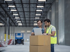 Workers using laptop and cell phone in warehouse