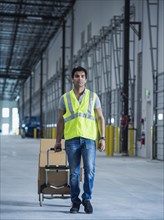 Indian worker pulling box on hand truck in warehouse
